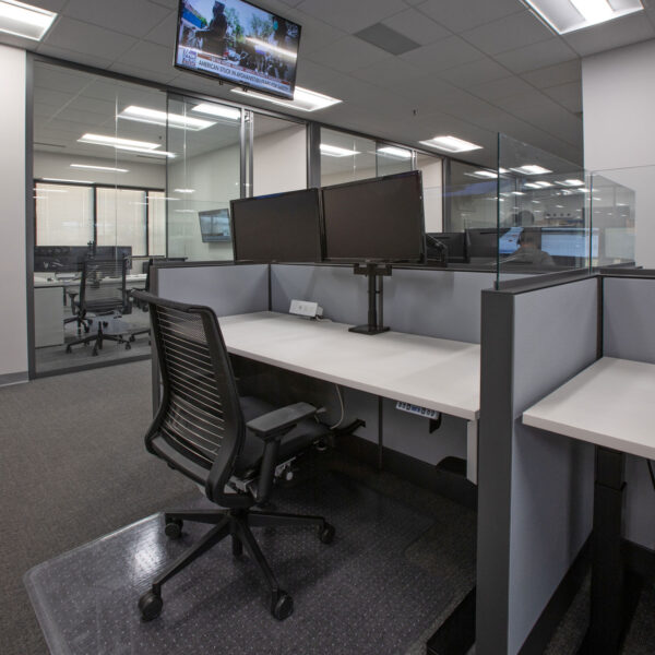 Cubicle with height adjustable desk, fabric panels with glass tops, and a task chair