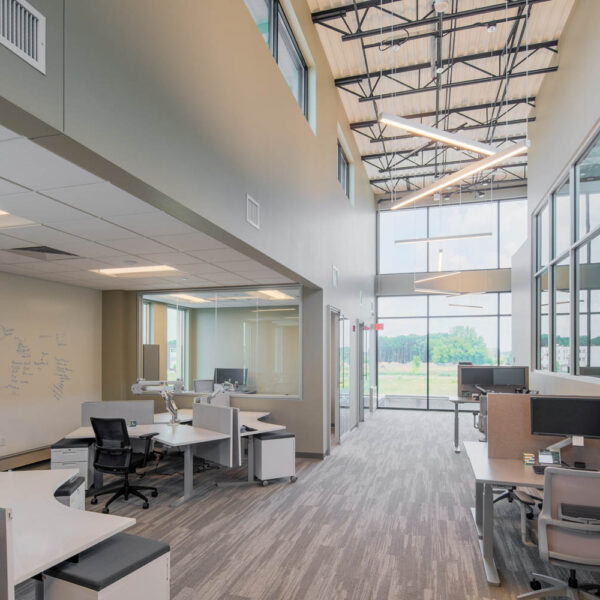 High ceiling office area with glass walls to let in light, height adjustable desks in multiple configurations, and a wall painted to be used as a whiteboard