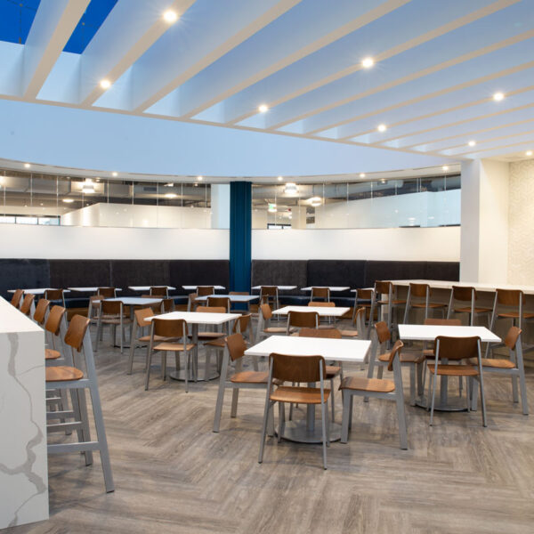Bright open café with communal tables, booth seating, and a patterned accent wall, featuring modern workplace furniture at the YMCA office