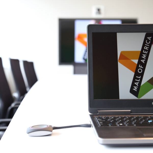 laptop on conference table showing click share device to cast laptop content onto tv