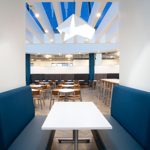 Contemporary break area with blue booth seating and white tables under geometric pendant lighting at the YMCA office café