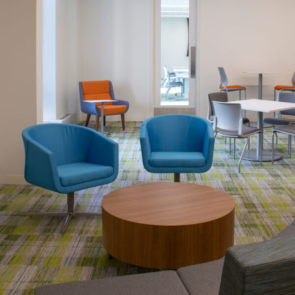 Colorful employee break room with blue and orange lounge chairs, patterned carpet, and natural light creating a bright, inviting workspace at the YMCA