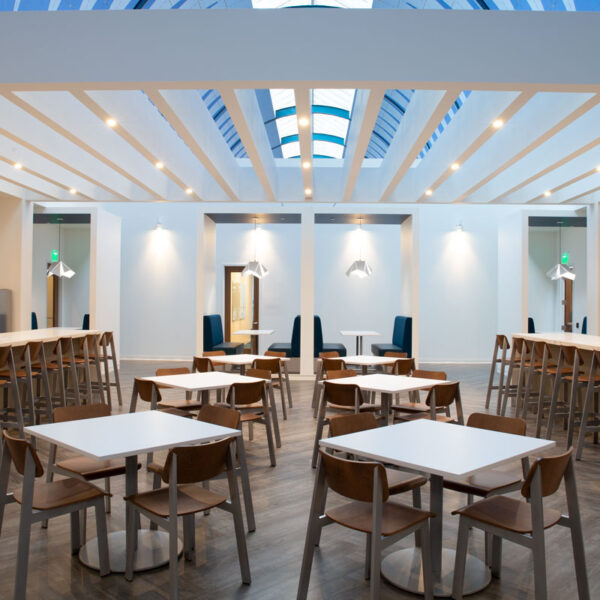 Contemporary office café with marble counters, wood chairs, blue booth seating, and skylit ceiling designed for social connection and collaboration at the YMCA