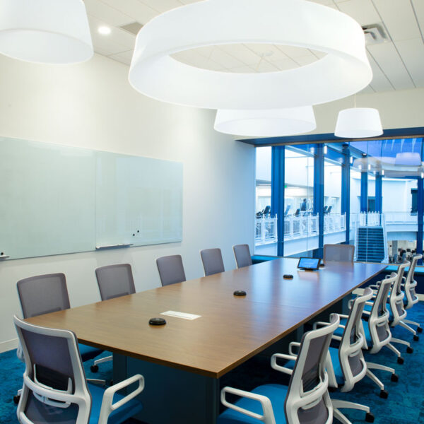 Spacious conference room with long wood meeting table, ergonomic task chairs, and large windows overlooking the YMCA atrium for a modern, collaborative meeting environment