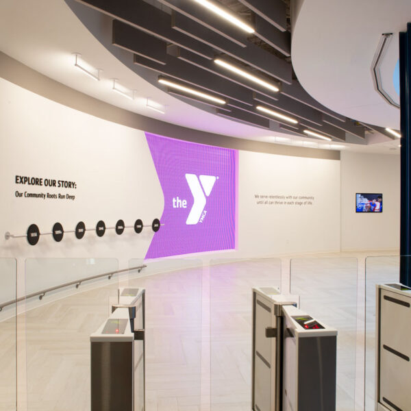 entry lobby featuring branded wall graphics, illuminated signage, and security turnstiles designed for a welcoming and professional visitor experience