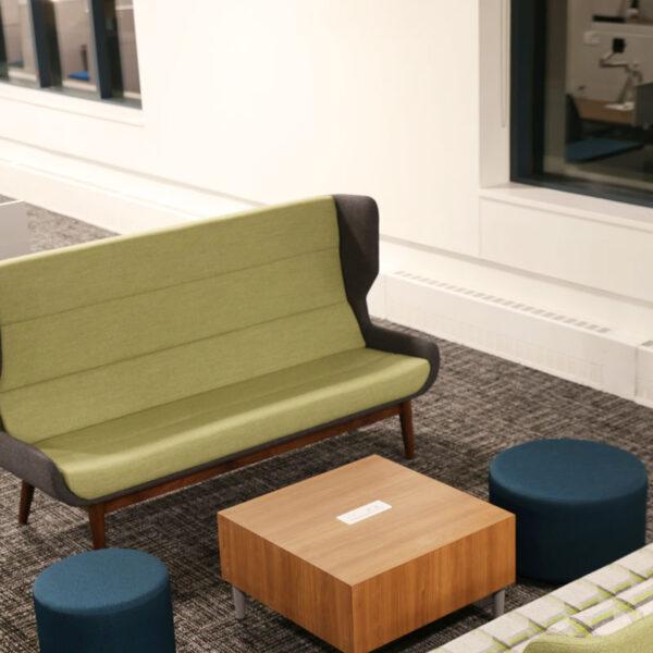 Comfortable office lounge with green sofas, blue ottomans, and a wood coffee table in a collaborative seating area at the YMCA headquarters